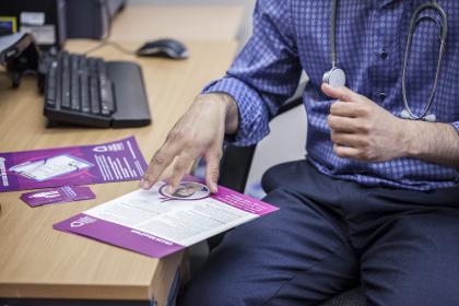 A GP using his hands to talk through a Target Ovarian Cancer leaflet on his desk