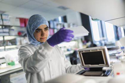 A female ovarian cancer researcher wearing a headscarf, purple gloves and a lab coat using equipment