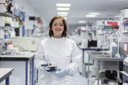 An ovarian cancer researcher smiling and holding lab equipment