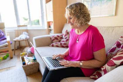 A person in a pink tshirt sitting on the sofa reading her laptop screen