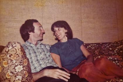 Caroline and her husband Ralph when they were younger sitting on a sofa smiling at each other
