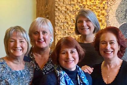 Five women all standing next to each other smiling