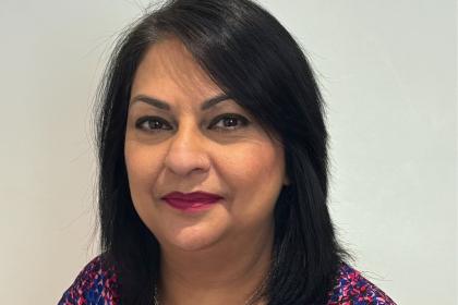 A headshot image of Sbba smiling towards the camera wearing a patterned purple top