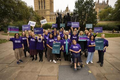 A group of Target Ovarian Cancer campaigners standing in the gardens in front of Westminster Parliament 