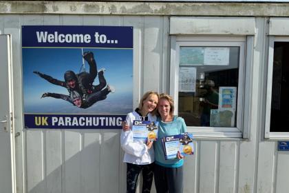 Two women with their arms around each other in front of UK Parachuting's office holding up  their certificates