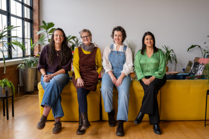 A photo of four women who have all had an ovarian cancer diagnosis sitting on the back of a sofa together all smiling