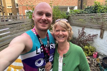 A selfie of Lewis and his mum Janet both smiling. Lewis is wearing his Target Ovarian Cancer running vest and his London Marathon medal