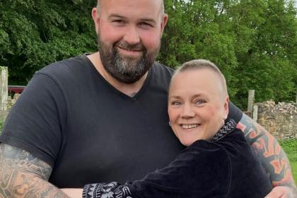 A photo of Adam and his wife Shelley cuddling and smiling. They are both wearing black tops and have their arms around each other
