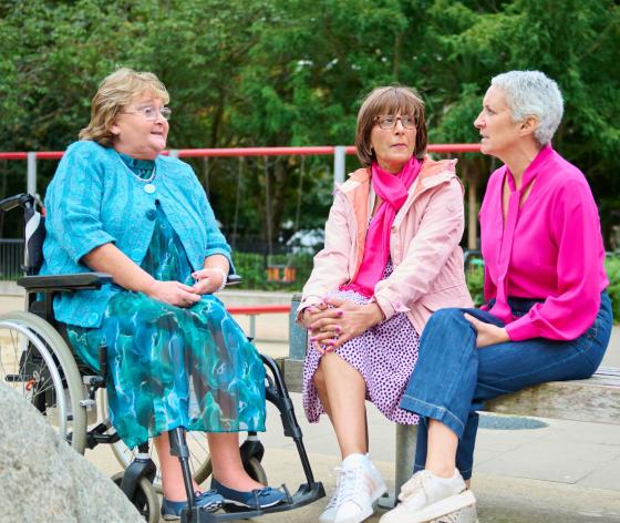 Three women sitting together outside, one in a wheelchair