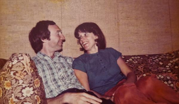 Caroline and her husband Ralph when they were younger sitting on a sofa smiling at each other
