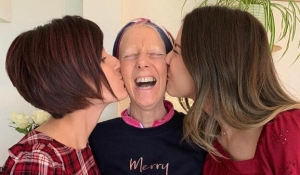 Gaby and Chloe standing either side of their mum Amanda kissing her cheeks whilst Amanda has a huge smile
