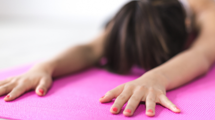 A woman with painted nails in a relaxed yoga position on a pink mat