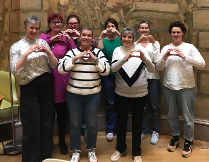 A group of 8 women all standing making a heart symbol with their hands