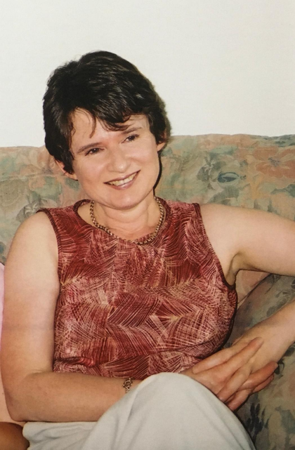 A photo of Julie smiling looking away from the camera, wearing a red patterned top and she has short dark brown hair