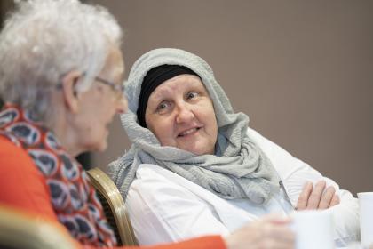 A woman with ovarian cancer wearing a head covering talking to another woman