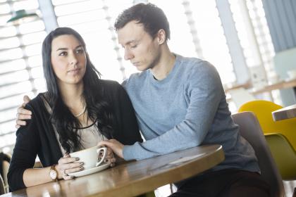 A man comforting a woman while having a cup of coffee