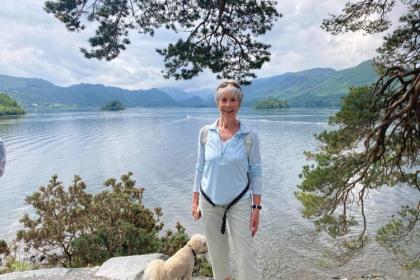 Lesley standing by a lake out walking with her dog