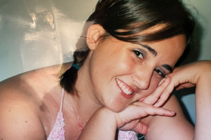 A photo of Leanne with her face resting against her hands and smiling