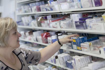 An image of a person working in a pharmacy taking a box of pills from the shelf