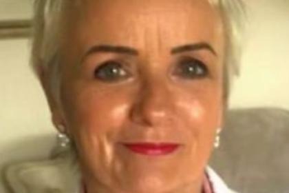 Pauline, a woman with short blonde hair smiling to the camera wearing a pink shirt and white jacket
