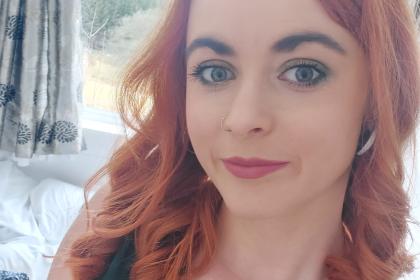 A selfie of Lucy with red curled hair and a teal green top on 