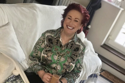 Alison smiling sitting on the sofa holding a cup of tea