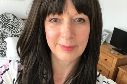 Gillian with long dark hair and a fringe taking a selfie, she's wearing her wig she named "Cher" 