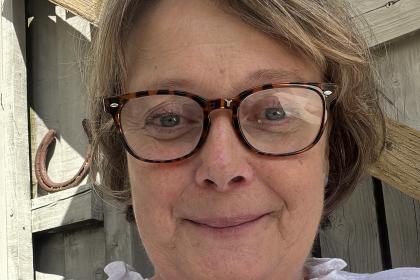 Libby sitting outside smiling wearing a white shirt and glasses