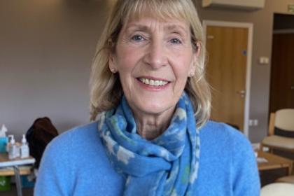 A photo of Sue smiling wearing a blue long sleeved top and blue patterned scarf
