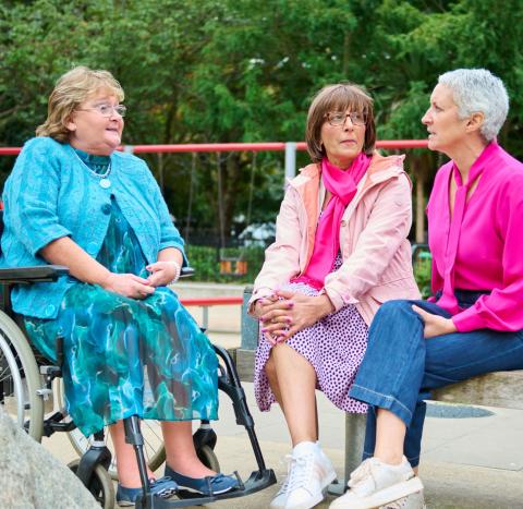 Three women sitting together outside, one in a wheelchair