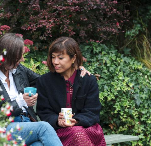 Two women sat on a bench in a garden