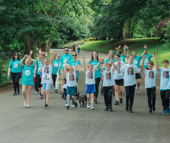 A large group of fundraisers holding their arms in the air as they take part in the Ovarian Cancer Walk|Run