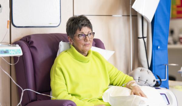 A woman in a green jumper having chemotherapy looking thoughtful