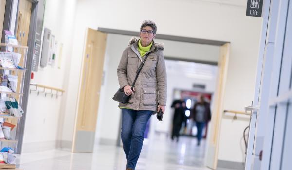 A woman with ovarian cancer wearing a coat and green jumper walking down a hospital corridor
