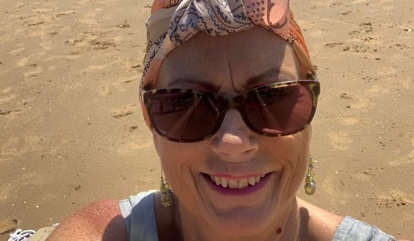 Jeanette taking a selfie on the beach, smiling wearing sunglasses and a headscarf