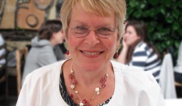 Delia smiling wearing glasses, and printed top and a white cardigan