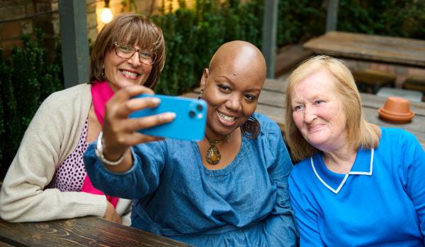 A photo of three women all smiling sitting on a bench taking a selfie together