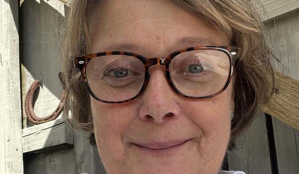 Libby sitting outside smiling wearing a white shirt and glasses