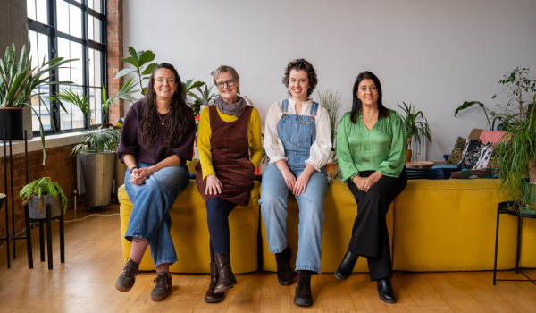 A photo of four women who have all had an ovarian cancer diagnosis sitting on the back of a sofa together all smiling