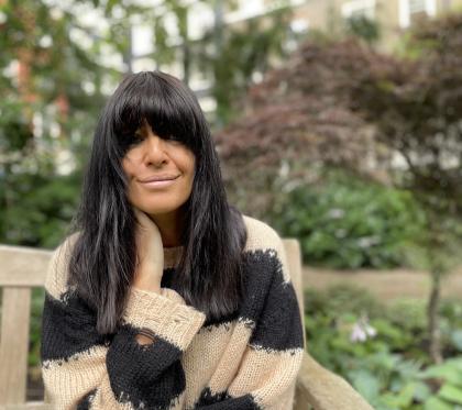 Claudia Winkleman sitting on a park bench looking into the camera