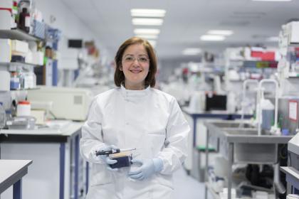 An ovarian cancer researcher smiling and holding lab equipment