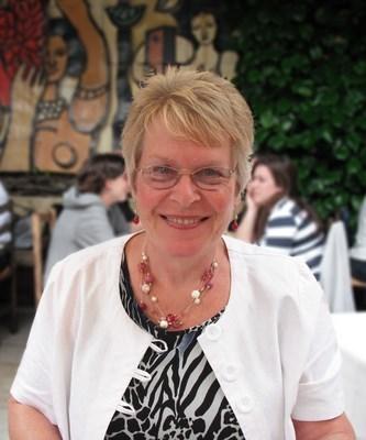 Delia smiling wearing glasses, and printed top and a white cardigan