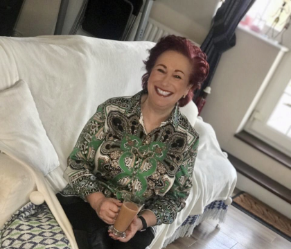 Alison smiling sitting on the sofa holding a cup of tea