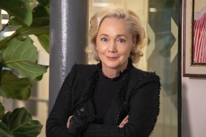 A photo of Emma Kane with blonde short hair wearing a black blazer looking towards the camera