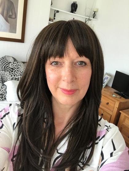 Gillian with long dark hair and a fringe taking a selfie, she's wearing her wig she named "Cher" 