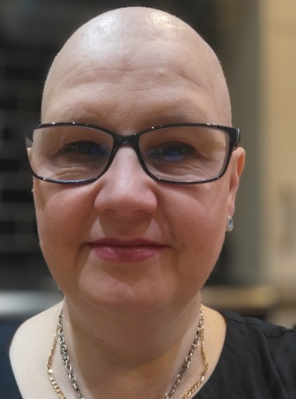 Jennifer during chemotherapy with no hair, she's softly smiling and wearing black glasses