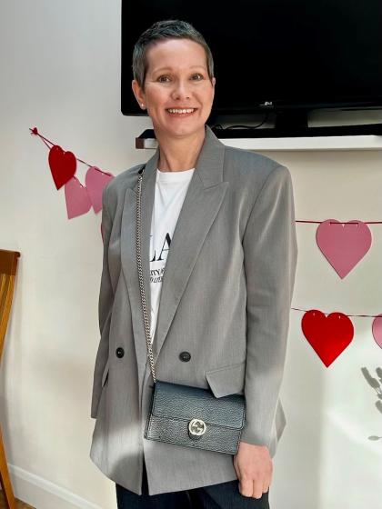 Sarah with short hair wearing a grey blazer and white tshirt smiling