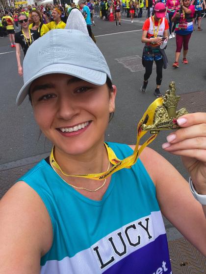 Lucy after running a half marathon holding her medal up. She's wearing a Target Ovarian Cancer running vest and a cap