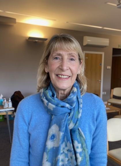 A photo of Sue smiling wearing a blue long sleeved top and blue patterned scarf