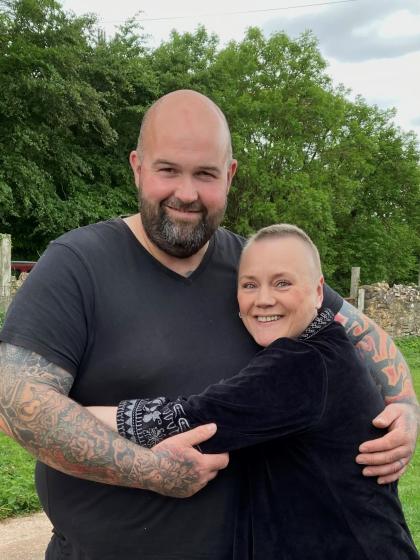 A photo of Adam and his wife Shelley cuddling and smiling. They are both wearing black tops and have their arms around each other